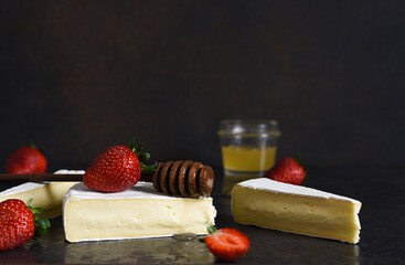 Brie cheese with strawberries and honey on a black kitchen table. Snack. Horizontal focus.
