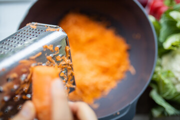 Female hands firmly grating a carrot into a bowl