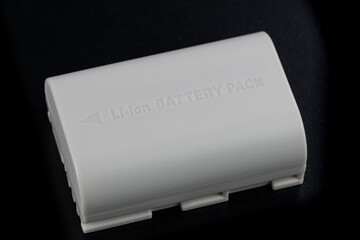 Eine weiße wiederaufladbare Lithium-Batterie (Li-ion Battery / Akku) liegt auf einem schwarzen...