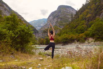 Naklejka na ściany i meble Yoga classes in nature. A woman does yoga in the mountains, near a mountain river flows. The concept of playing sports alone. Social exclusion