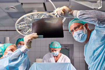 medical workers in hospital examine x-ray prints during operation, caucasian medics consult with each other while looking at x ray image, medicine, surgery, healthcare concept