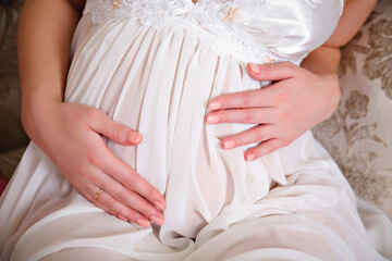 Happy pregnant woman sitting in a transparent negligee and touching her stomach. The concept of waiting for a baby and a happy pregnancy