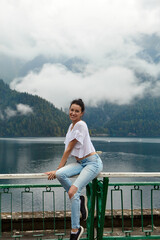 A girl in white clothing on a background of a mountain lake with blue water and mountains with clouds. Background.