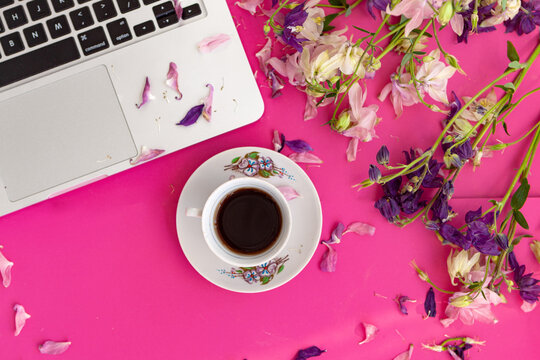 Home office desk. Female workspace with laptop and coffee mug, flowers and petals on pink background. Flat lay, top view. Fashion blog look. Add your text.