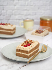 A piece of a light layered genoise sponge coffee cake topped with caramel almond in a plate with fork and coffee cup in background. It made with whole egg cake and butter 