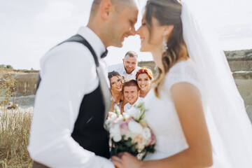 Happy newlyweds kiss on the background of friends