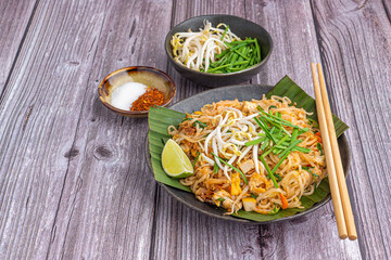 Pad Thai served with vegetables and lemon slice on banana leaves on a black plate on a wooden table. Thai food is famous. Top view with space for text. Concept of Thai traditional foods