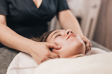 Obraz na płótnie Canvas Technique for performing a facial massage in a beauty salon - hands of a professional masseur - rejuvenation and relaxation of facial muscles