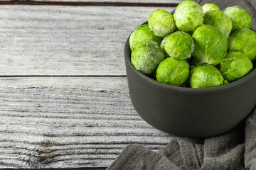 Frozen brussels sprout in the bowl and napkin on gray wooden table. Horizontal orientation. Copy space.