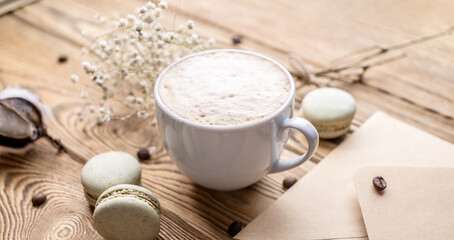 Cup of aromatic coffee and macaroons and an envelope on a wooden table. Concept of a cozy atmosphere and nice breakfast
