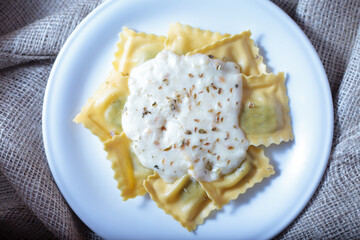 Ravioli fresh pasta dish with cheese sauce and oregano served on a white plate over warm textured piece of cloth