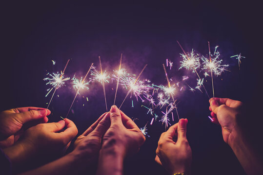 Cropped Hands Of People Holding Sparklers At Night