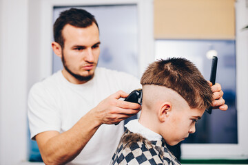 Fototapeta premium Hairdresser barbershop parihopher strechot small boy sitting on a chair