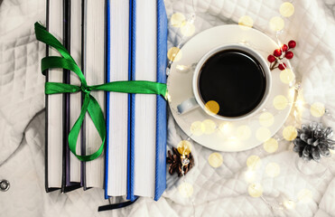 A stack of books tied with a green ribbon are on a light background near a white Cup of coffee and bokeh. Light background with cones on it. The concept of comfort