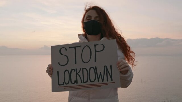 Stop Lockdown woman protest holds hands cardboard with sign Game Over in covid-19 medical mask against background blue sunset sky in evening in winter. Quarantine. Lockdown. Coronavirus. Epidemic