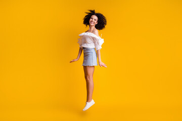 Fototapeta na wymiar Full size photo of adorable positive brunette woman jumping wear white top blue skirt sneakers isolated on yellow color background