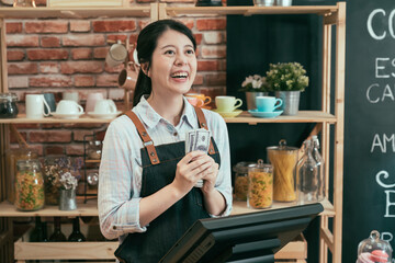 Close up portrait of smiling happy girl waitress holding bunch of money standing in cafe counter. female barista in apron laughing with lots of cash in hands after working in coffee shop all day