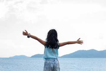 Asian little girl stands and stretches the arms breathe in the fresh air while traveling by sea on holiday.