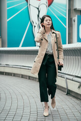 Obraz premium straight photo full length asian korean woman walking on bridge in modern osaka city. nippon runner billboard in background. beautiful lady flicks hair wearing high heels shoes on overpass outdoors.