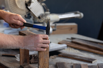 man hand is hammering nail on wood desk in workshop with construction background