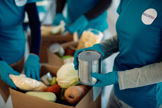 Unrecognizable volunteers packing donated food in cardboard boxes.