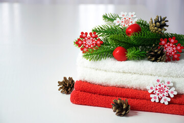 Stack of red and white towels with fir branches, red toys, snowflakes and pine cones on white table. SPA massage or beauty salon, relaxation and salfe care in Christmas or New Year variant.