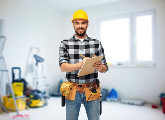 profession, construction and repair concept - happy smiling male worker or builder in helmet with clipboard over room with building equipment background