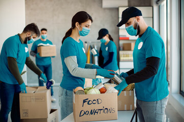 Group of volunteers with face masks packing donated food in cardboard boxes.