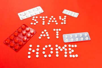 Stay home lettering from round white pills on a red background. Packs of pills. High quality photo