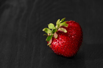 one strawberry on a black wooden background