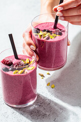 Berry smoothie with nuts in woman hands, light gray background. Healthy detox drink concept.