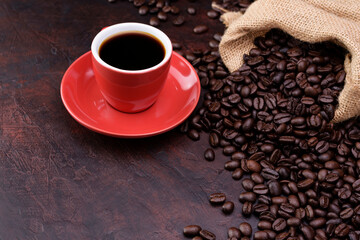 Red coffee cup with black needle coffee with saucer and fragrant roasted coffee beans on the needle colored table - top view with copy space.