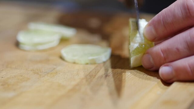 Woman cutting lime into two halves. Cuts green lime with a knife on a wooden cutting board. Cooking process. Healthy ingredients for delicious meal. Close up of man's hands slicing green lime, slow mo