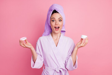 Portrait of pretty amazed cheerful girl wearing turban holding in hands new daily day cream product isolated on pink pastel color background
