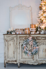 Christmas tree on wooden chest of drawers commode bureau in white interior, decorated with artificial flowers, garlands and toys