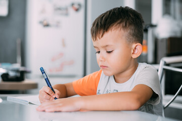 a boy is learning to write the letter K in a notebook preparing for school
