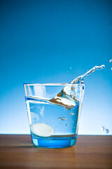 Blue glass of water splashing with a dissolving pill inside.