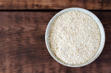 Squeezed white sesame in bowl on wooden background. Benne oilcake. Top view.