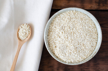 Squeezed white sesame in wooden spoon and in bowl on wooden background and linen. Benne oilcake. Top view.