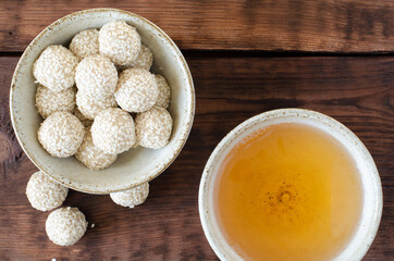 Handmade sesame sweet balls and green tea in bowl on wooden background. Top view.