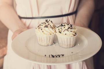 cupcakes with white cream decorated with balls of confectionery powder in the hands of a woman in a pink dress.