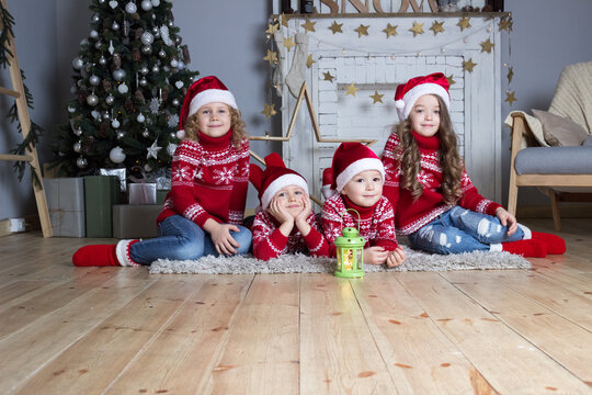 Four little santa hat kids in christmas sweaters sitting near new year decorated fireplace. Xmas celebration card. Holiday greeting. 
