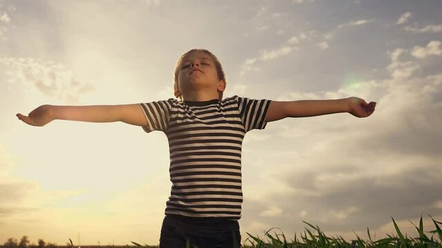 Happy kid praying in the park. Kid in a field with wheat praying raised his hands to the sides. Happy child closing his eyes looks to the sky. Child prays to the sky childhood dreams. Spiritual prayer