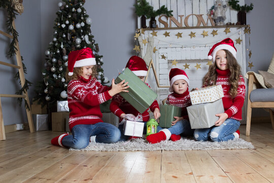 Merry christmas celebration santa hat kids in red sweaters opening gift boxes near new year decorated fireplace. Xmas children invitation card. Holiday greeting
