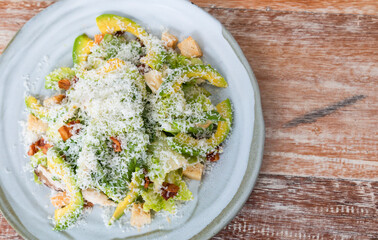 Avocado salad with vegetables, chicken and bacon in a white vintage plate. Close up view of mixed vegetable, avocado salad with bread crumb, grilled chicken and bacon. 