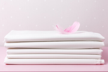 A stack of folded clean white sheets with a pink feather on the table.