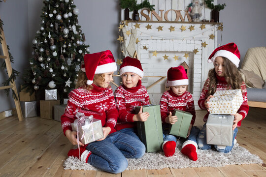 Merry christmas celebration santa hat kids in red sweaters opening gift boxes near new year decorated fireplace. Xmas children invitation card. Holiday greeting