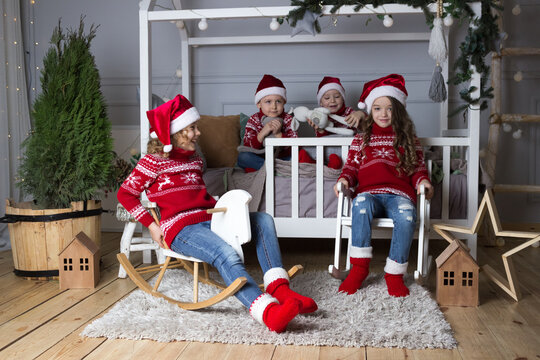 Merry christmas celebration happy kids in santa hats, red sweaters, socks sitting on bed and rocking horse, chair. New year decorated room. Xmas children invitation card. Holiday greeting