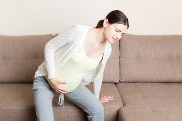 Fototapeta premium The expectant mother suffers from back pain and tries to sit on the sofa