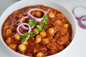 Closeup view of chole masala also known as channay, chana is an indian street food made of chickpeas, chopped tomatoes, ghee and cumin decorated with red onion rings and green parsley served in bowl